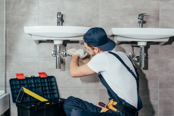 back view of young professional plumber fixing sink in bathroom